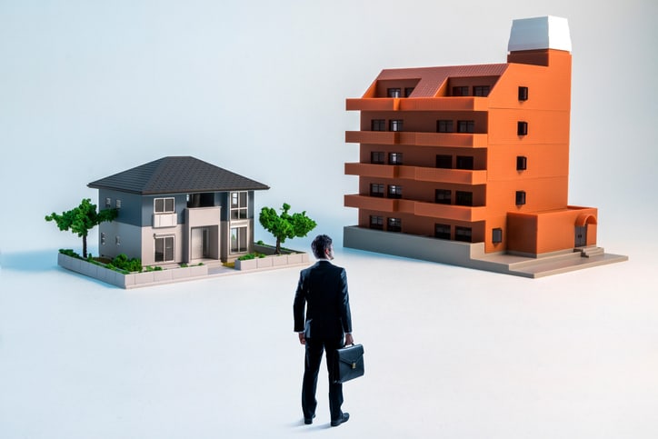 businessman looking at a house and a apartment building.