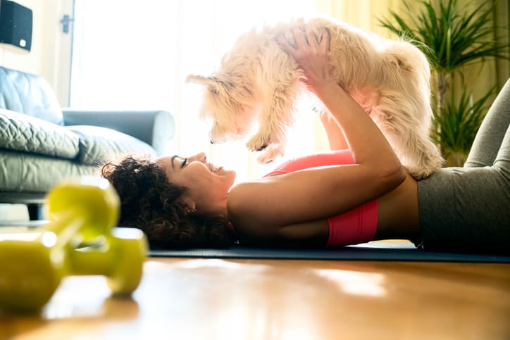 Young girl in sportswear playing with her dog at home - Sporty woman training fitness workout indoor - Animals, sport and recreational concept