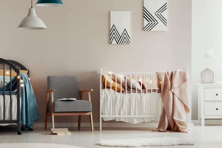 Fashionable retro armchair between two wooden cribs in cute twins nursery
