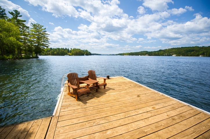 Adirondack chairs sitting on a wooden dock facing a lake during a sunny day
