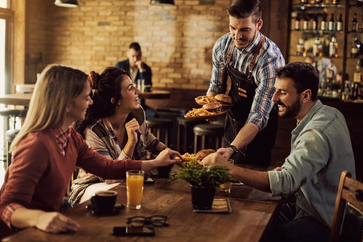 Happy waiter serving food to group of friends in a pub.