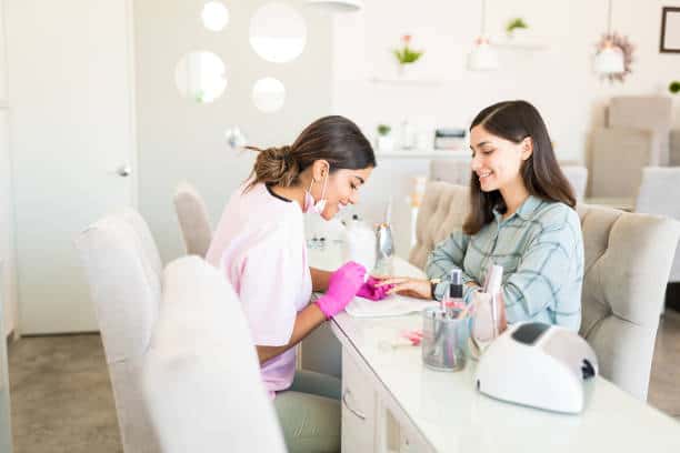 Smiling manicurist decorating nails with color on client's hand at beauty spa