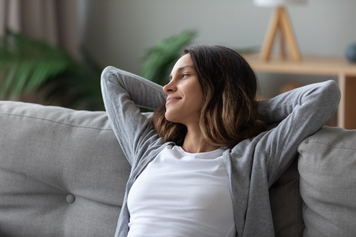 Tranquil pretty woman in casual home clothes put hands behind head leaned on couch resting in living room looking away smiling feeling serenity. Take break, keep calm, mood and free lazy time concept