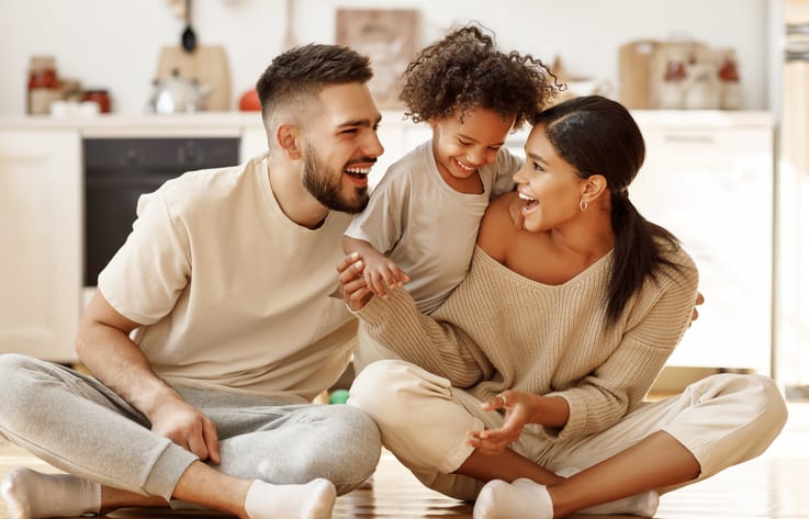 happy family multiethnic mother, father and son laughing, playing,and tickles on floor in cozy kitchen at home